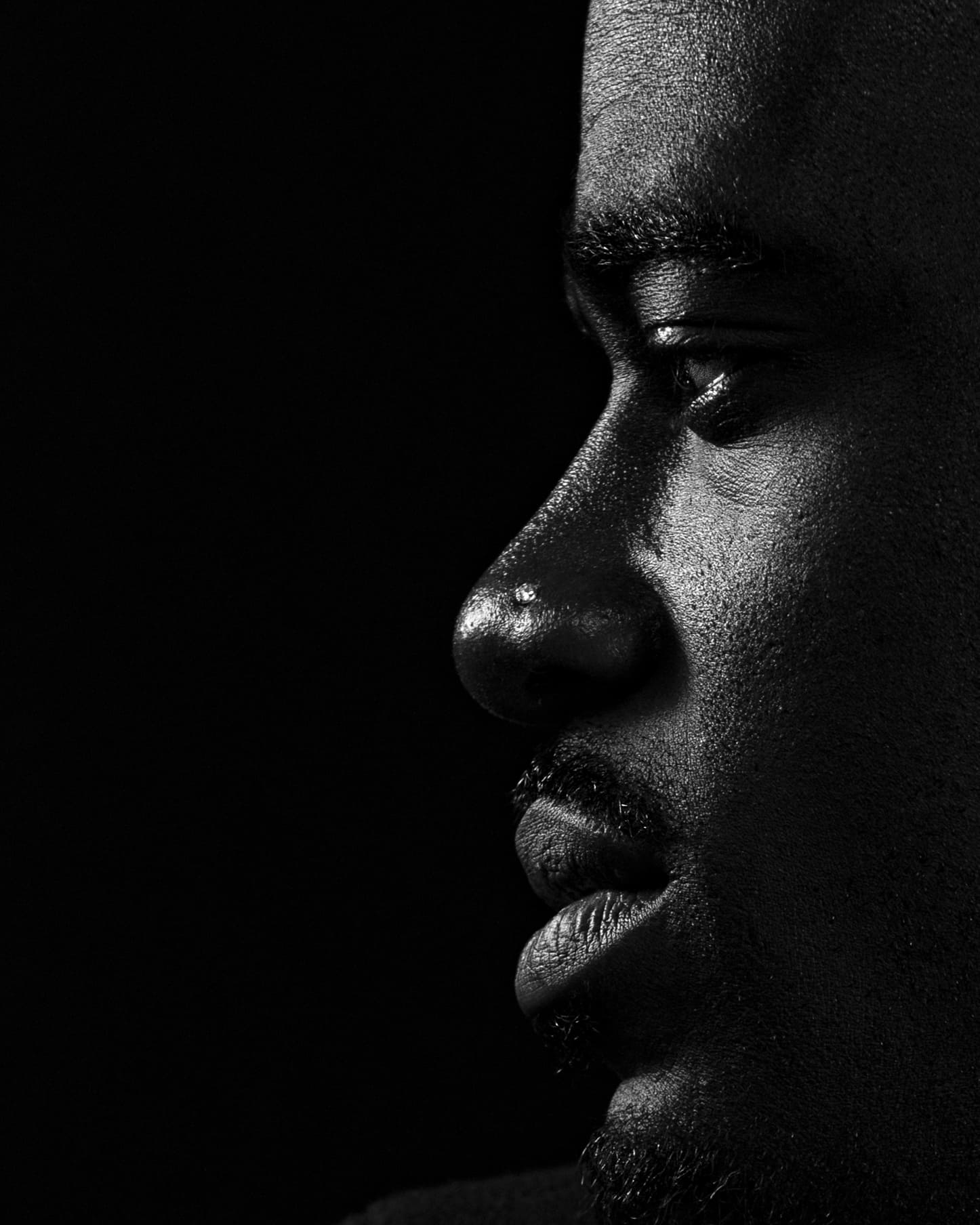 Black and white side profile of a bearded Black man against a solid black background.
